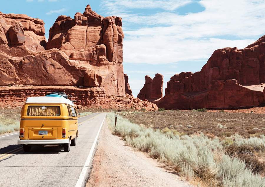 A vintage camper van on a desert road through red rock formations
